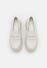 White leather loafers with a rounded toe, beige chunky sole, and decorative top strap featuring a cut-out detail. Branding on the insole.