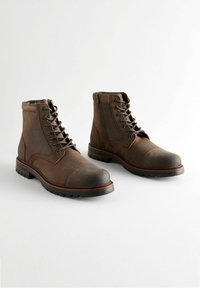 Botas de tobillo de cuero marrón con cordones y cremallera lateral. Punta redonda, superficie texturizada, suela de goma con surcos y acentos de costura en contraste.