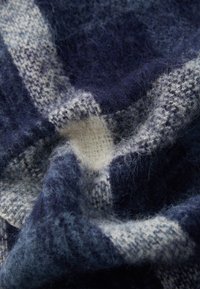 Ulltekstil med et blått og hvitt rutemønster og en myk, fluffy tekstur. Stoffet er lagt drapert, og viser dybde og rikdom.