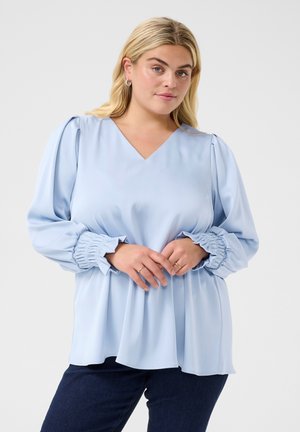 Světle modrá blůza vyrobená z hladkého materiálu, s výstřihem do V, nabíranými rukávy a uvolněným střihem, který se mírně stáčí na lemu.
