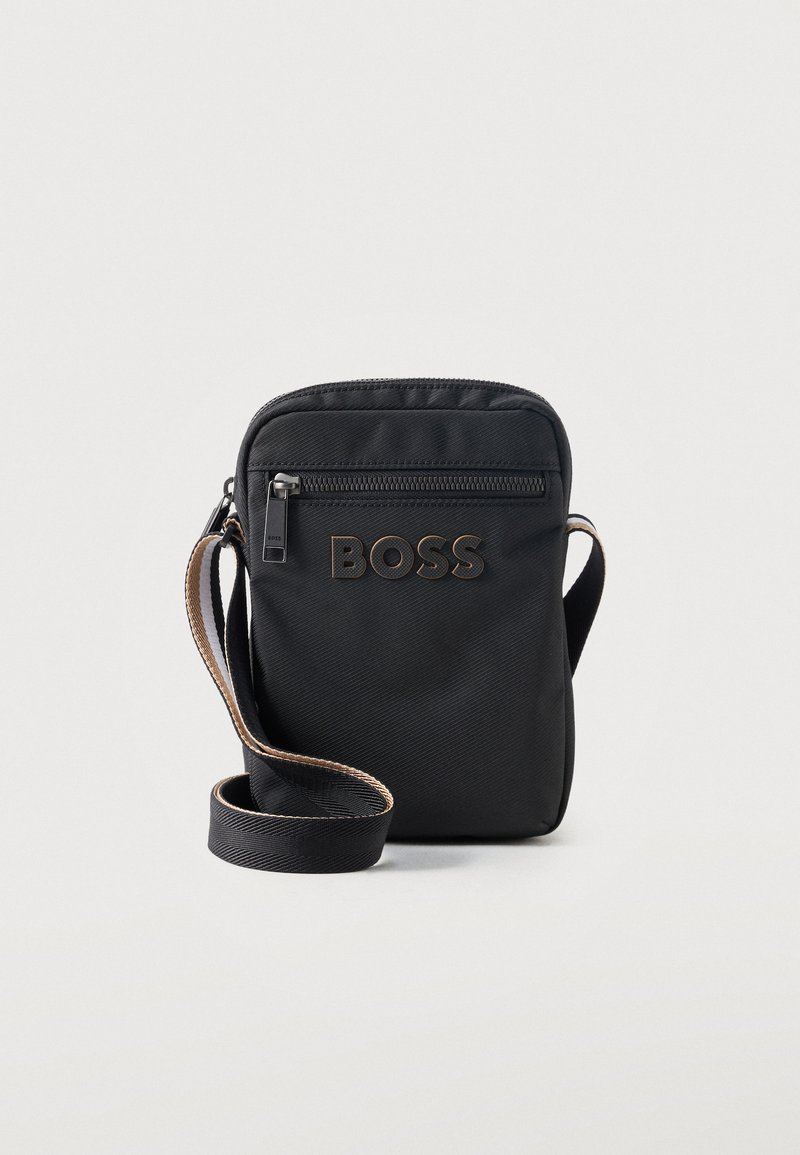 Μαύρη τσάντα ώμου με μπροστινή θήκη με φερμουάρ και λογότυπο "BOSS", ρυθμιζόμενο λουρί με καφέ περιγράμματα, σε ανοιχτό φόντο.