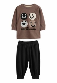 Braunes Langarmshirt mit vier Smileys und dem Text "LÄCHEL, JEDER TAG IST GLÜCKLICH", kombiniert mit schwarzen elastischen Hosen mit Gummibund.
