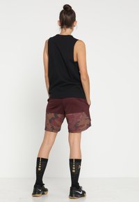Schwarzes ärmelloses Top, burgunderfarbene und camouflagemusterte Shorts mit Taschen, kombiniert mit schwarzen knielangen Socken mit goldenen Akzenten.
