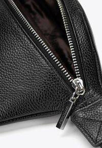 Černá texturovaná kožená taška se stříbrným zipem a úchytem. Interiér má tmavou podšívku. Zip je kovový s viditelnými zuby.