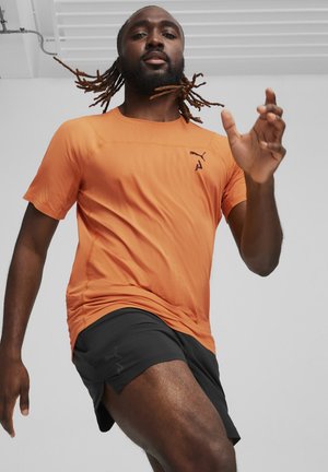 Orange sports t-shirt med korte ærmer og rund hals, parret med sorte shorts. Inkluderer et logo på både t-shirten og shortsene.