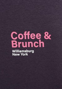 "Kaffe & Brunch" i stora rosa bokstäver med "Williamsburg New York" i mindre vita bokstäver på en mörk stickad tygbakgrund.