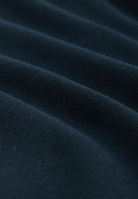 Tessuto blu scuro con trama testurizzata e costine diagonali visibili, che mostra una superficie morbida e liscia con una sottile lucentezza dovuta al riflesso della luce.