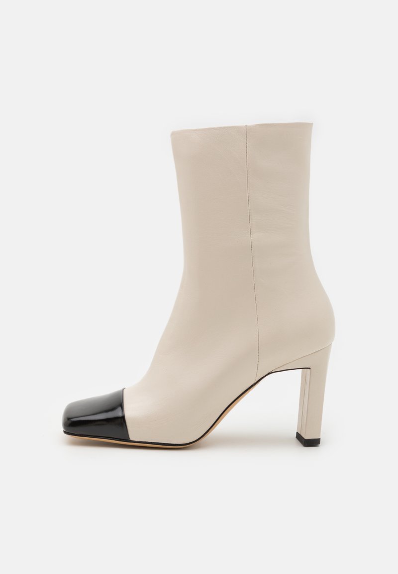 Beige nahkasaapad musta lakknahast varvasotstega. Omab ruudukujulist kontsa, siledat tekstuuri ja minimaalset õmblusdetaili.