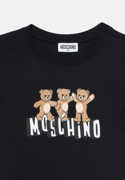 Chemise noire pour enfants avec trois ours en peluche beiges et espiègles au-dessus du logo "MOSCHINO" en lettres blanches majuscules sur le devant.