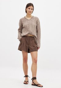 Bežinė kabelinė megztinė su V formos iškirpte, derinama su laisvomis rudomis šortais ir plokščiais sandalais. Pintas diržas puikiai papildo aprangos spalvų schemą.