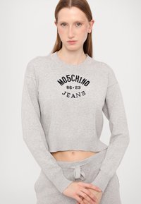 Sweater cinzento cortado com punhos e decote canelados. Logótipo bordado preto "Moschino Jeans 86.23" na frente. Material têxtil suave.
