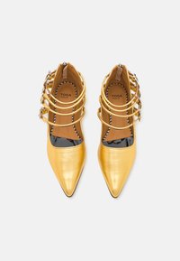 Gold metallic pointed-toe shoes with a glossy black patent leather accent. Features multiple gold bands across the top. Brand name visible inside.
