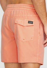 Helle korallenfarbene Badeshorts aus einem glatten Stoff, mit einem elastischen Bund, einer Gesäßtasche mit Klappe und gestickten Details.