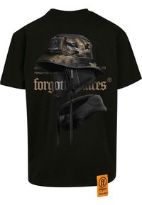 Juodas marškinėliai su spausdintu kamufliažo kibiriniu skrybėle ir stilizuotu tekstu. Audinys atrodo minkštas, o fasonas standartinis, etiketė oranžinė ant apvado.