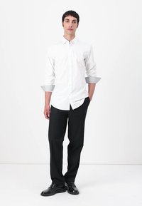 Camisă albă cu guler clasic, cu manșete în carouri contrastante, asociată cu pantaloni negri. Cămșa are un design ajustat.