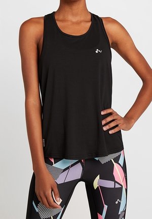 Woman wearing sleeveless black athletic tank top and high-waisted leggings with colorful geometric patterns, standing with one hand on hip.