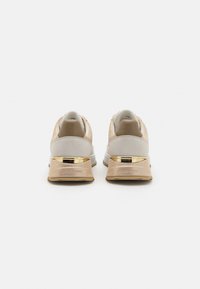 Sportsneakers met een beige en grijze bovenkant, gouden accent op de hiel, en een gewatteerde witte zool; van textuur suede en glad leer.