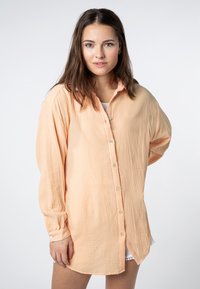 Pfirsichfarbener, übergroßer Button-Up-Hemd aus strukturiertem Stoff, mit klassischem Kragen, langen Ärmeln und Seitenschlitzen am Saum.