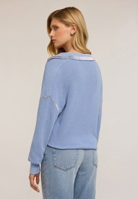 Maglione lavorato a maglia di un blu chiaro con una vestibilità comoda, motivo testurizzato e dettagli in accento argentato sul colletto e sulle spalle.