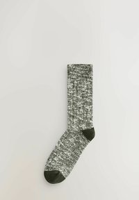 Stricksocke in dunkelgrün und weißem Melange-Muster mit ribbeltem Bündchen, verstärkter Zehe und Ferse. Weiche Textur, knielange Länge.