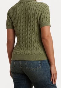Pletené polokošile s krátkým rukávem v olivové barvě s kablovým vzorem, s žebrovaným límečkem a lemem, spárované s džíny, zobrazené ze zadního pohledu.