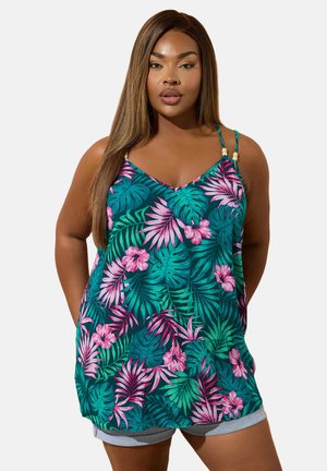 Femme portant un haut sans manches bleu sarcelle avec des motifs de feuilles et de fleurs tropicales roses et vertes, assorti à un short gris clair.