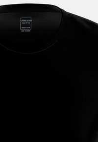 T-shirt in cotone organico nero con scollatura rotonda e una superficie liscia. I dettagli del tag includono il nome del marchio, il materiale e il paese di produzione.