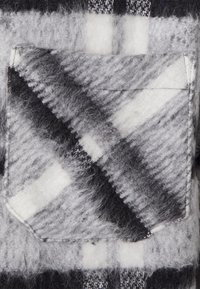 Tecido de lã xadrez em preto, branco e cinza, com um bolso cosido que apresenta um padrão xadrez diagonal e costura visível.