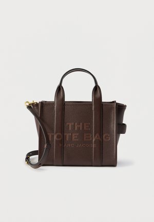 Borsa tote in pelle marrone scuro con effetto granuloso, manici superiori, tracolla staccabile e testo in rilievo "THE TOTE BAG MARC JACOBS" sul davanti.