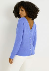 Suéter lavanda con cuello en V y tejido texturizado, con cierre de botones en la parte trasera y mangas largas, combinado con pantalones blancos.