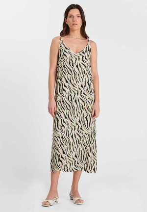 Donna che indossa un vestito senza maniche di lunghezza media con stampa astratta zebra in nero, verde e beige, in piedi contro uno sfondo bianco semplice.