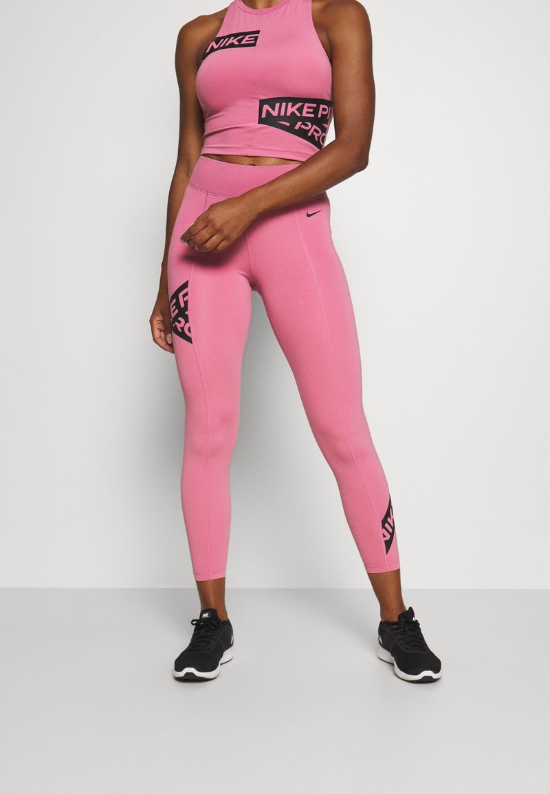 Top corto deportivo rosa y leggings con marca Nike en negro, diseño ajustado, material elástico y costuras planas. Zapatillas deportivas negras.
