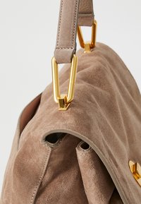 Tan suede handbag with a smooth texture, featuring a gold metal hardware accent and a flat strap for shoulder carry.
