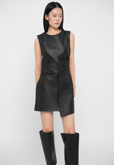 Fekete, ujjatlan bőrruha aszimmetrikus kialakítással, gyűrt oldalakkal és elöl cipzárral. A megjelenést térd fölé érő fekete bőr csizmák teszik teljessé.