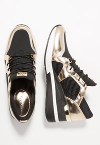 Czarne i metalicznie złote buty sportowe z siateczkowymi akcentami, amortyzowaną podeszwą i eleganckim klinowym fasonem z kontrastującymi teksturami.