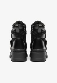 Fekete bokacsizmák textil és bőr anyagokból, vastag gumitalppal, pántokkal és texturált felülettel az oldalakon.