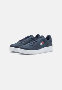 Sneakers in pelle blu navy con suola in gomma bianca, punta rotonda e dettagli perforati. Presentano un patch con il logo del marchio in rosso, bianco e blu.