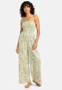 Monos verde claro, sin tirantes, con un cuerpo fruncido, piernas anchas y un estampado botánico de hojas en tonos crema y melocotón. Textura suave.