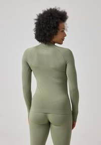 Langärmliges sportliches Oberteil in Olivgrün, das ein figurschmeichelndes Design mit strukturiertem Stoff, Daumenlöchern und einem dezenten Logo auf dem Rücken aufweist.
