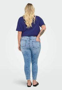 Zili džinsu skinny bikses ar nolietu mazgāšanu, piecām kabatām un subtīlām tamborējuma detaļām. Kombinētas ar purpura īsām piedurknēm.