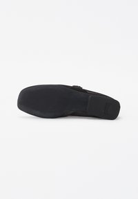 Semelle de chaussure noire avec bout carré et petit talon carré, texturée pour une meilleure adhérence, présentée sur un fond blanc.