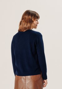 Marineblauer Wollpullover mit Rundhalsausschnitt, gerippten Säumen und Abschluss; getragen über einem braunen Lederrock. Verfügt über eine lässige Passform und strukturierte Oberfläche.