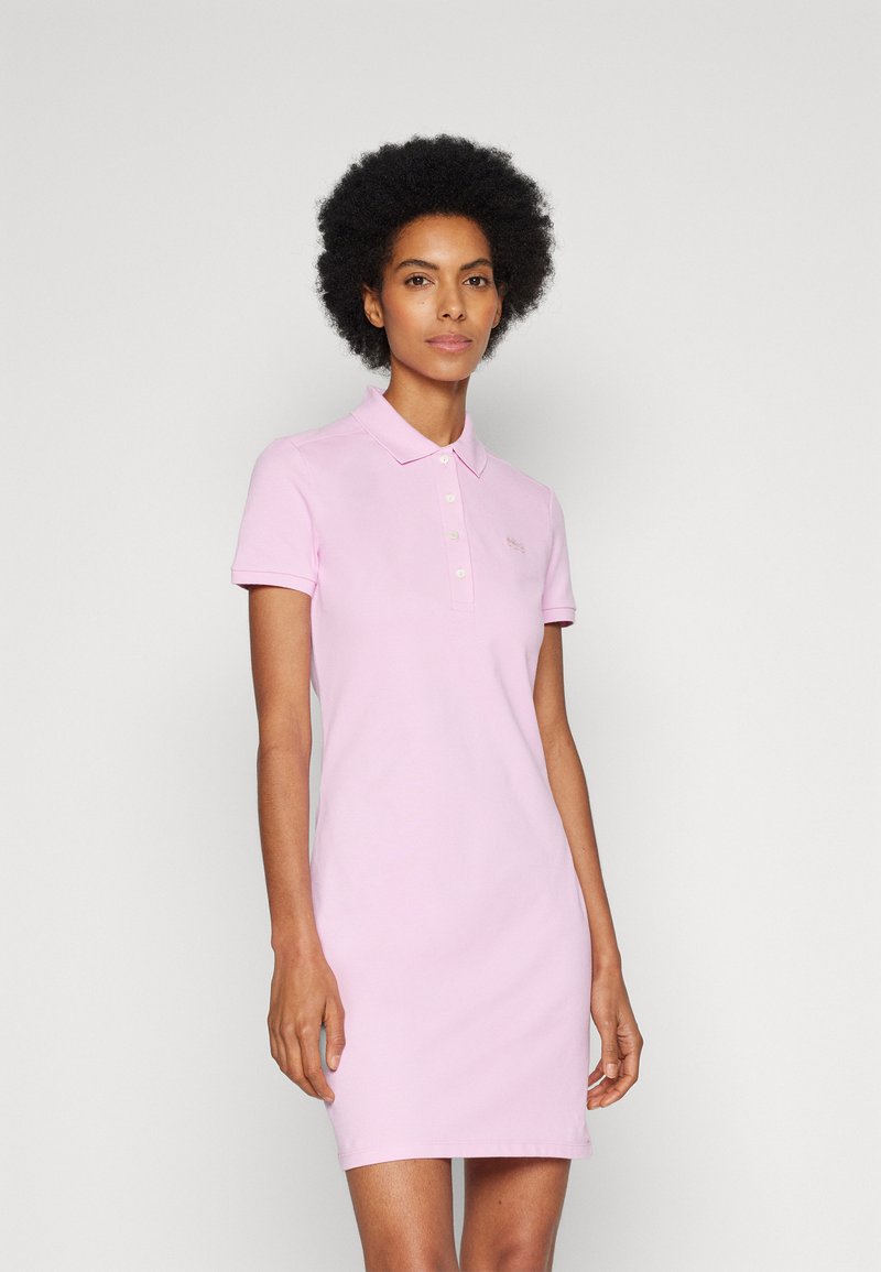 Vestido polo rosa hecho de algodón, con mangas cortas, un cuello y un placket de botones. Textura suave con una forma ajustada.