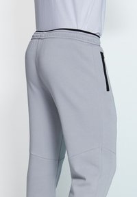 Helle graue Sweatpants aus weichem Stoff, mit schmalem Schnitt, elastischem Bund und einer Reißverschlusstasche an der Seite.