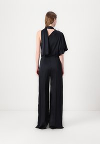 Macacão preto com design de um ombro; material satin leve; silhueta de pernas largas; textura subtil; estilo minimalista.