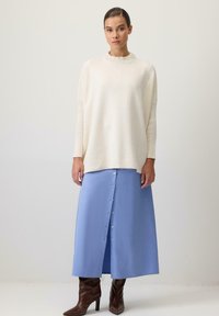 Gaišs krēmkrāsas oversized džemperis ar ribotu tekstūru, apvienots ar garu, gaiši zilu pogājamā svārku un brūnām ceļgala augstām zābakiem.