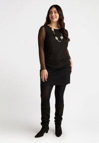 Svart långärmad topp med genomskinliga ärmar, draperad design; tillsammans med en svart kjol, svarta strumpbyxor och knähöga stövlar i mocka. Silverkedjesmycke.