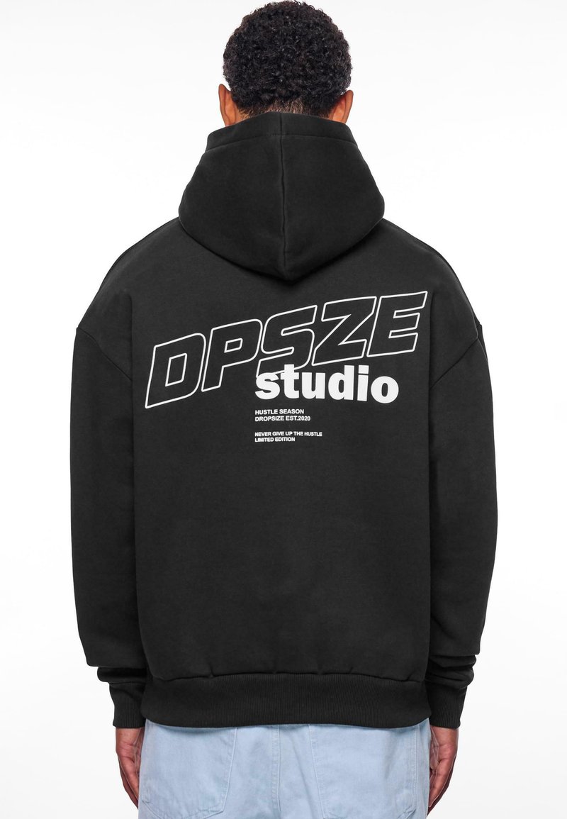 Czarna bluza z kapturem z dużym białym napisem na plecach "DPSZE studio" oraz dodatkowymi frazami poniżej. Wykonana z miękkiego materiału, z kieszenią typu kangur.