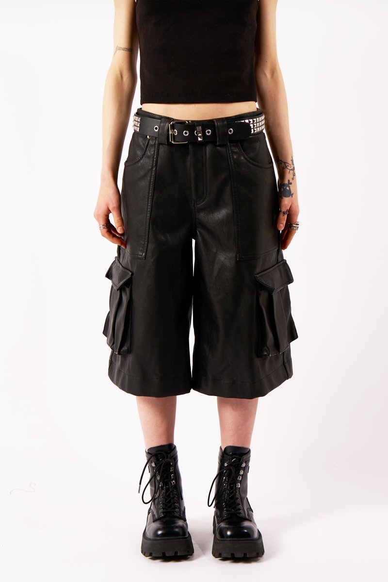 Melni ādas kargo šorti ar sānu kabatām, vidēja garuma, ar uzdurtu melnu jostu. Kombinēti ar melniem šņorējamiem potīšu zābakiem.