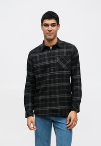 Camisa xadrez preta e cinzenta com botões, bolso no peito, mangas compridas e textura suave, combinada com jeans azul claro.